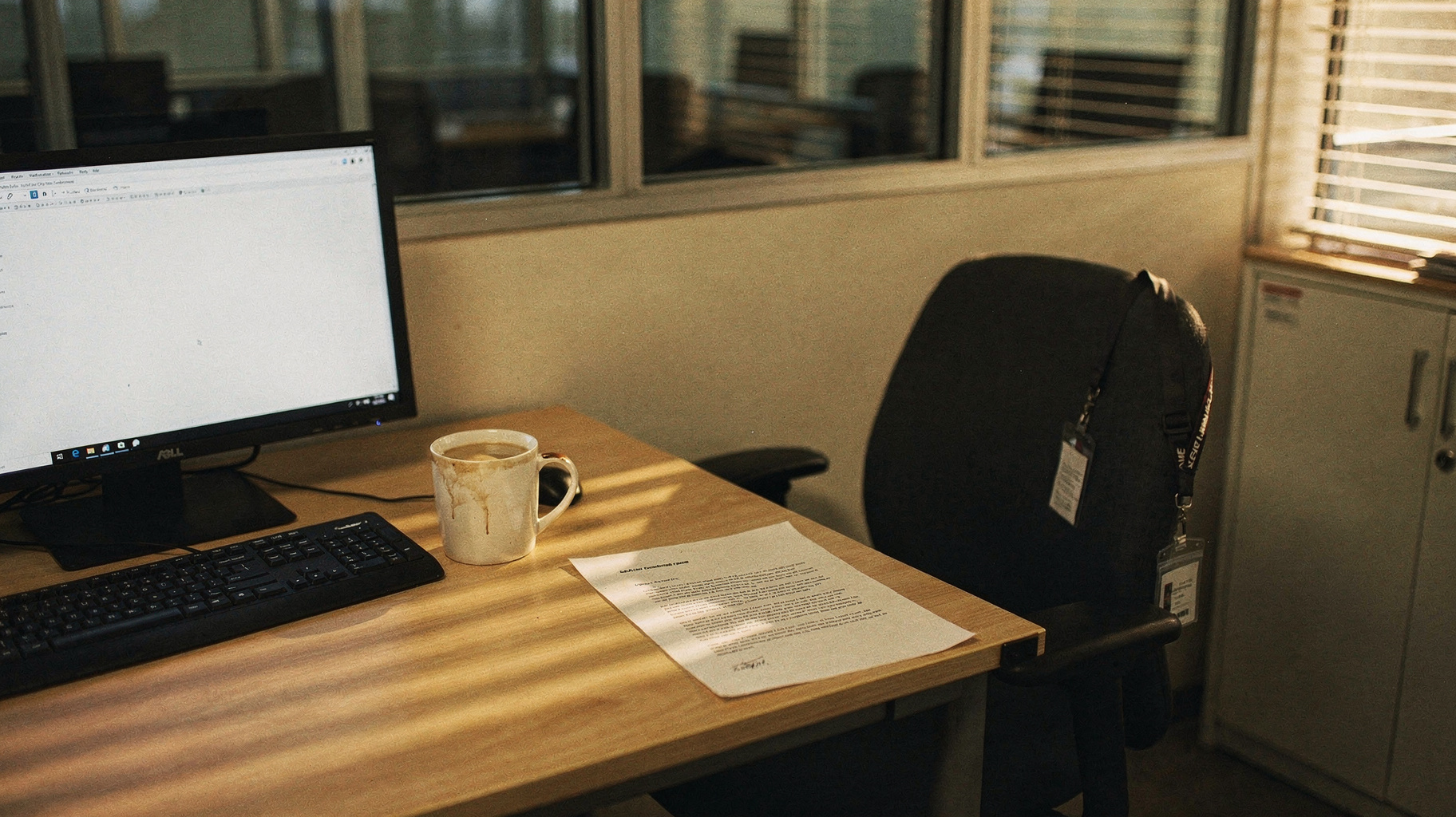 A documentary photograph of an empty office desk at a frontier AI lab, a keyboard and monitor left on, a resignation letter printed on plain paper lying beside a coffee mug, late afternoon light through blinds