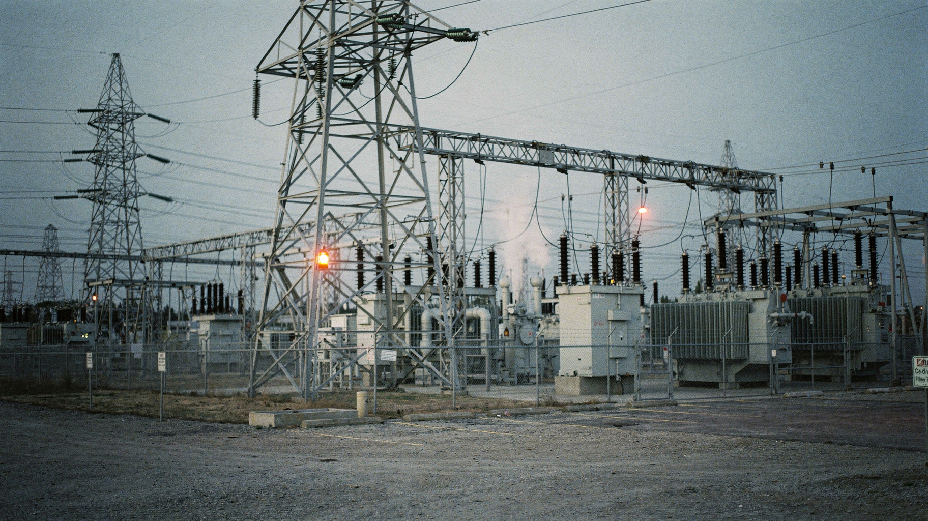 An electrical substation at dusk with transmission towers receding into haze, rendered as an archival darkroom print.