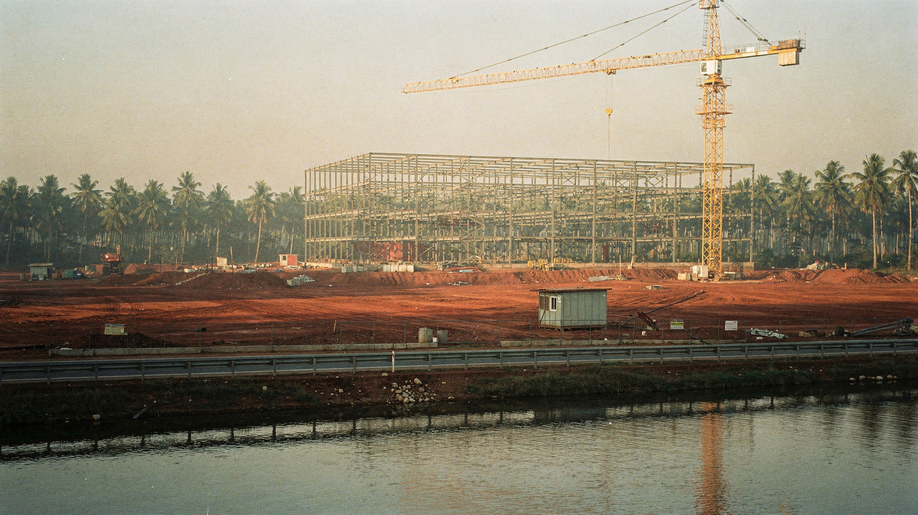 A data center construction site in tropical haze with steel frame rising from red earth