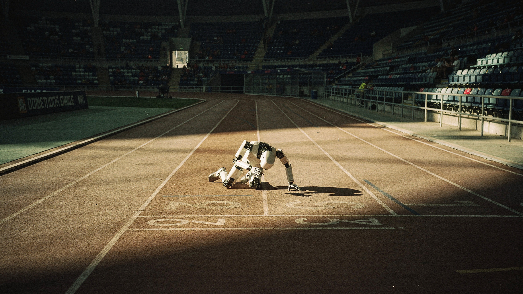 A humanoid robot collapsed mid-sprint on an indoor running track, folded forward at the waist near the finish line.