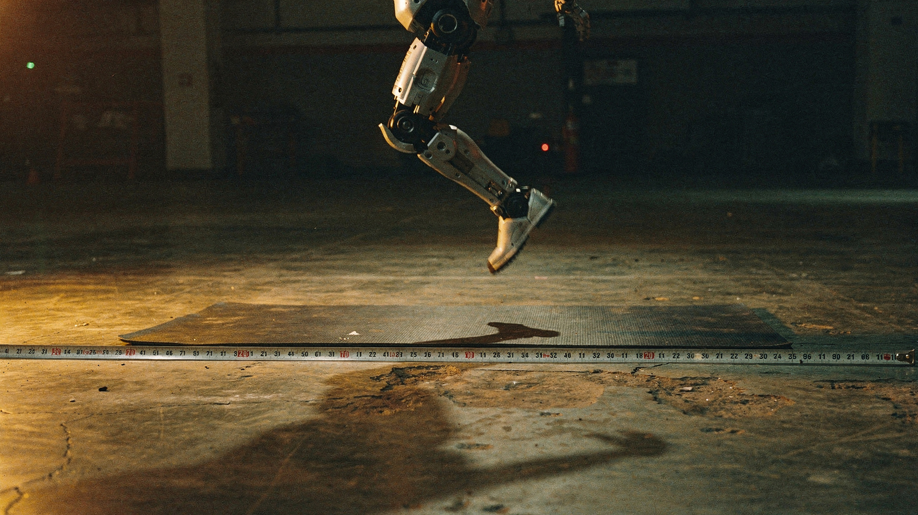 A humanoid robot frozen mid-leap in a dark arena, rendered as an archival darkroom print.
