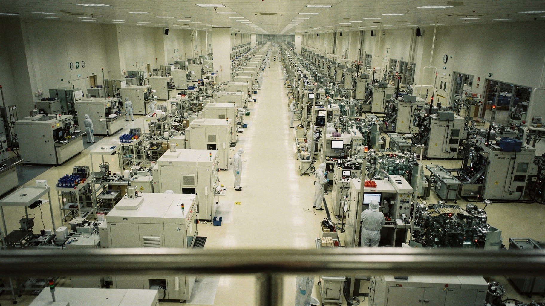 an archival darkroom print of a vast semiconductor fab cleanroom floor stretching to a raw concrete wall, hazmat-suited workers under amber sodium lights.
